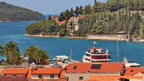 Eine Küstenstadt mit einem Gebäude mit rotem Dach, einem Boot, das an der Mole liegt, und einer Hügelkette mit Bäumen im Hintergrund.