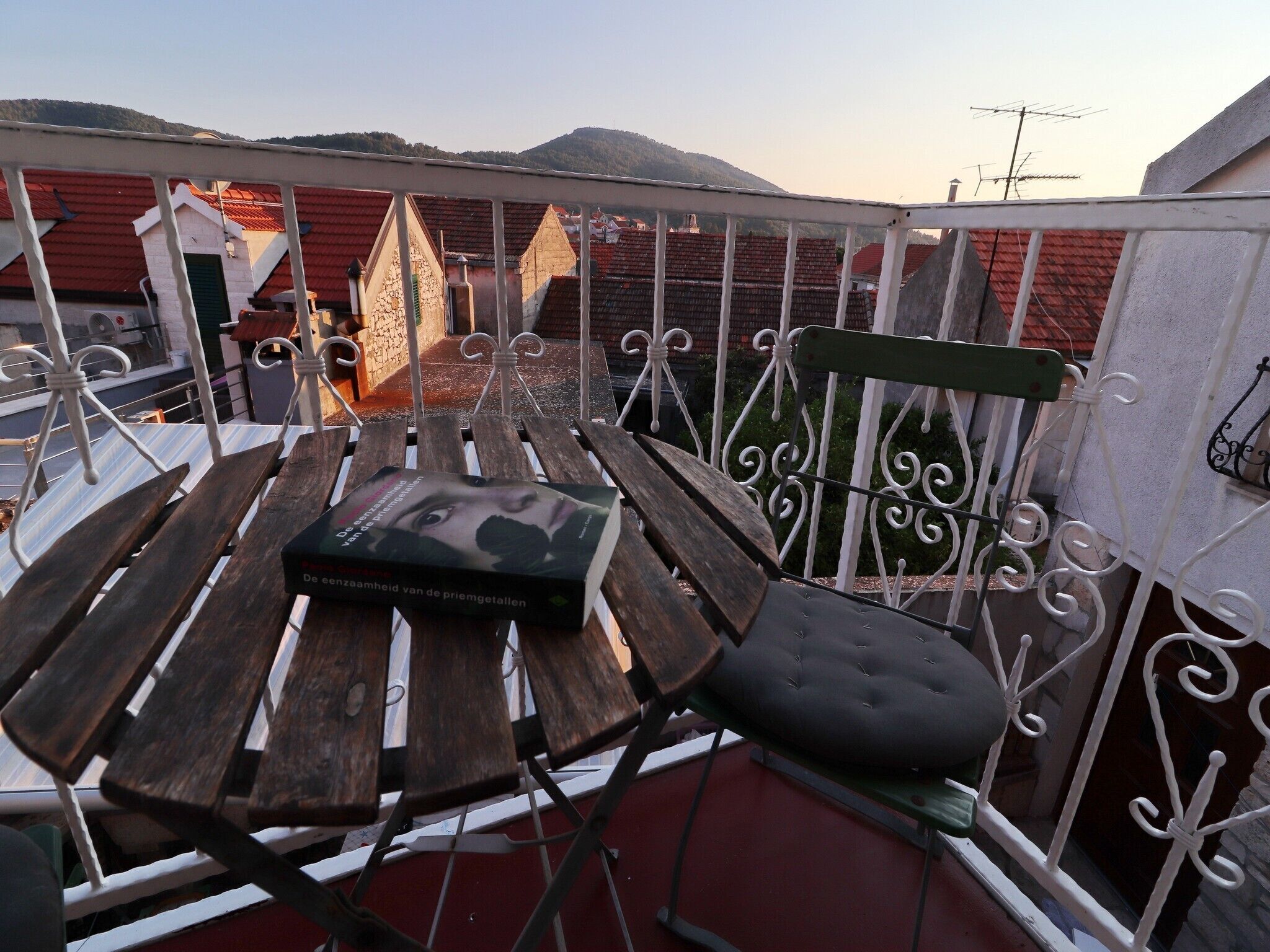 A balcony with a wooden table, a green cushioned chair, and a book titled "De conscientiousie van de priemgetalijen".