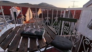 Un balcone con un tavolo di legno, una sedia imbottita verde e un libro intitolato 'De conscientie van de priemgetalijen'.