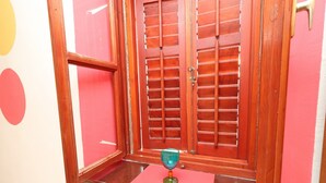 Una stanza con una finestra in legno e un piccolo tavolo con un bicchiere.