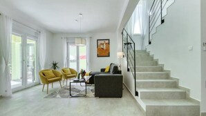 Un salon moderne avec un escalier, de grandes fenêtres et un tableau accroché au mur.