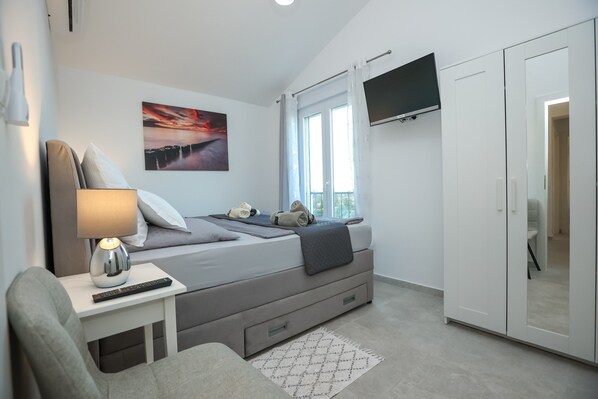 A modern bedroom with a bed, bedside table with a lamp, a TV mounted on the wall, and a wardrobe.