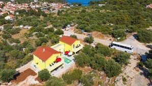 Vue aérienne d’une zone côtière avec un bâtiment jaune doté d’un toit rouge, une piscine et un autobus blanc garé à proximité.