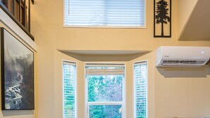 A dining room with a large wooden table, six chairs, and a view through a window with blinds.