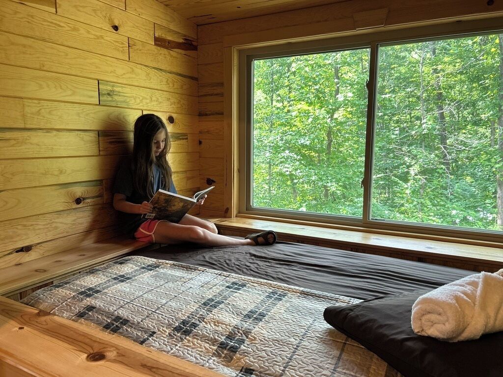 A room with a bed, a window, and a view of trees.