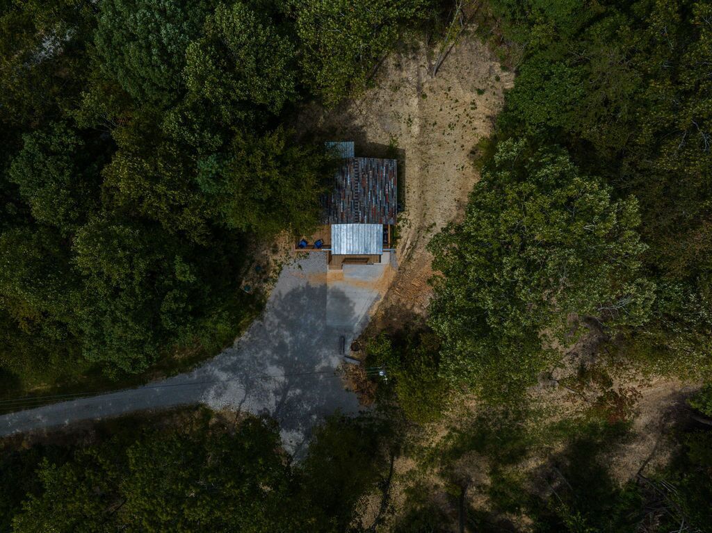An aerial view of a cabin surrounded by dense forest, with a dirt path leading to it.