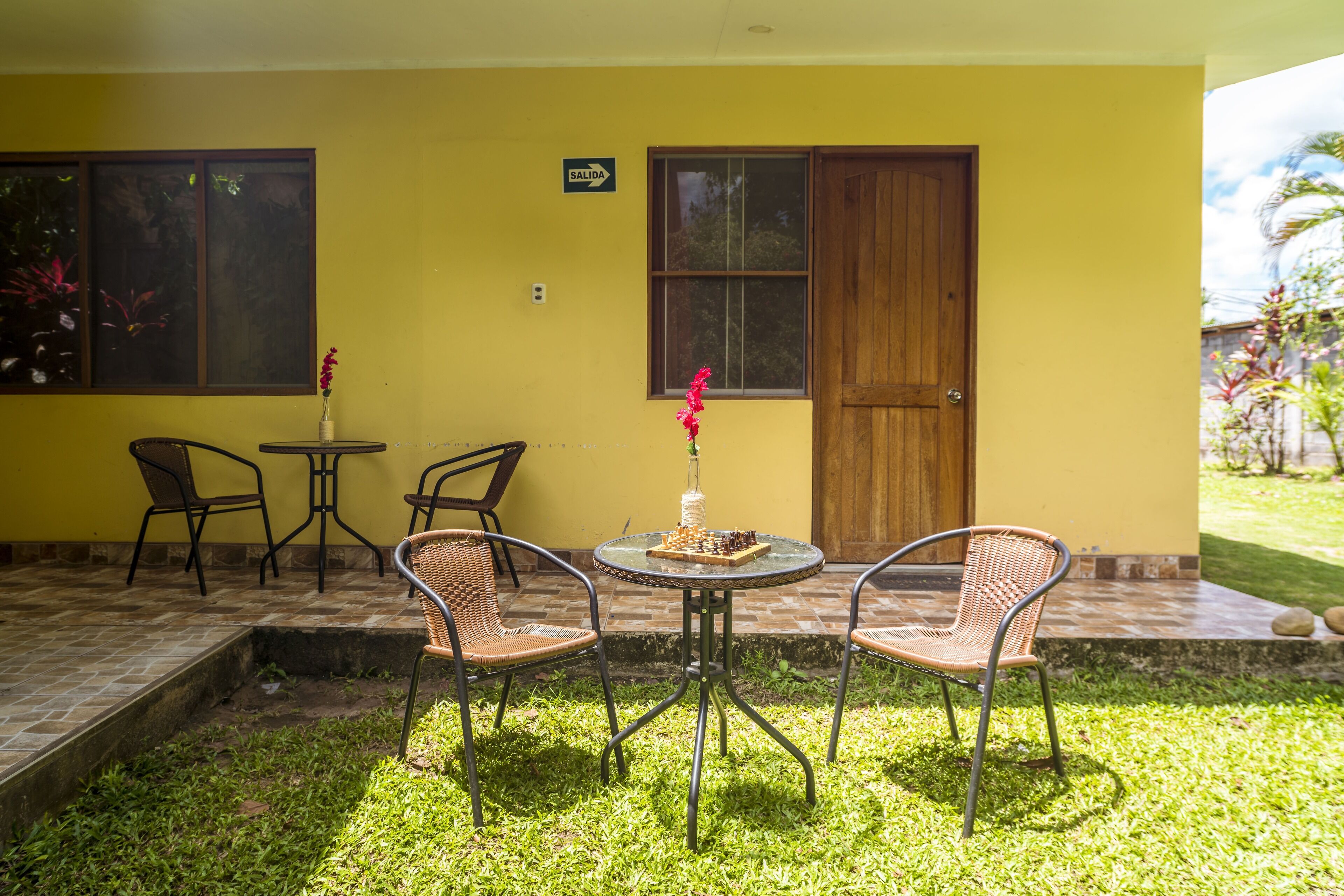 Un área de estar al aire libre con una mesa y sillas, una puerta de madera y una ventana con el letrero 'SALIDA'.