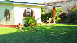 A single-story building with a sloped roof, a mural on the side, and a small garden area with a palm tree and chairs.