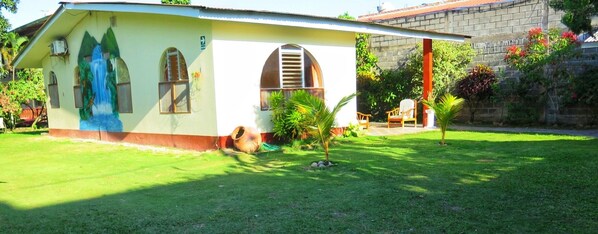 A single-story building with a sloped roof, a mural on the side, and a small garden area with a palm tree and chairs. - GoInn (Tarapoto)