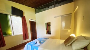 A bedroom with a bed, a window with curtains, a door, and a small mirror on the wall.