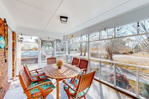 Relax in this sunroom with a large table and six chairs, surrounded by a beautiful view of the parking lot and trees.