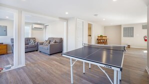 Een ruime woonkamer met een tafeltennistafel, banken en een houten eettafel.