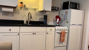 Een kleine keuken met witte kastjes, een zwart aanrecht, een magnetron, een koelkast en een koffiezetapparaat.