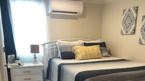 Een slaapkamer met een bed, nachtkastje, lamp en een stoel.