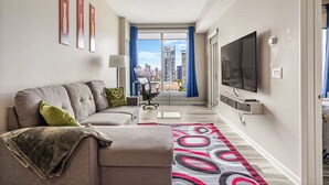Un salon moderne avec un canapé, un téléviseur et une vue sur le paysage urbain, visible à travers une grande fenêtre.