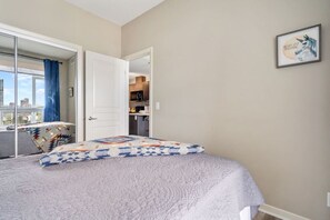 A bedroom with a bed, a door leading to a balcony, and a kitchen visible through an open door. - City Centre Retreat: 1BR Condo with Desk (Calgary)