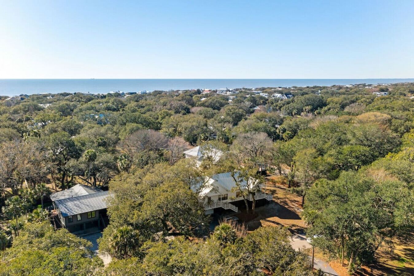 A coastal property with multiple houses surrounded by dense vegetation and a clear view of the sea.