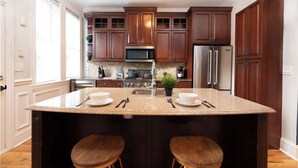 A kitchen with dark wooden cabinets, stainless steel appliances, a granite countertop, and two wooden stools. - Spacious House ~3min walk WrigleyField~Free Prkg (Chicago)