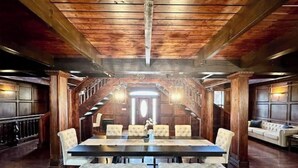 A spacious dining area with a long table, cushioned chairs, and a wooden ceiling.