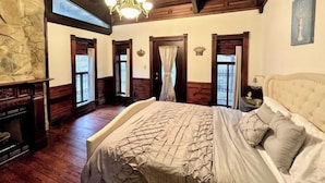 A bedroom with a large bed, wooden ceiling, stone wall, and a chandelier.