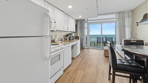 A modern kitchen with white cabinets, a dining area with a table and chairs, and a balcony with a view.