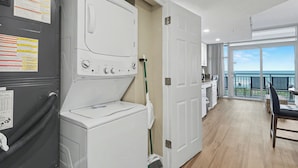 A laundry area with a washer and dryer, a mop, and a door leading to a balcony with a view.