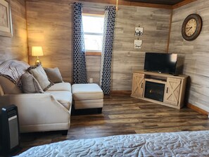 A cozy living room with a sofa, ottoman, TV, and fireplace. - Cozy Cottage Close To Mammoth Cave. Boat Ramp, Master Suite, Pergola, Peaceful.  (Cub Run)