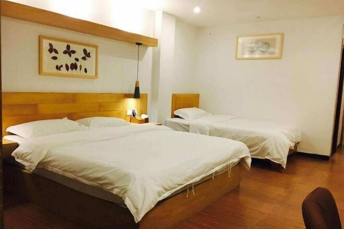 A hotel room with two beds, wooden headboards, a framed artwork on the wall, and a small table with a lamp.