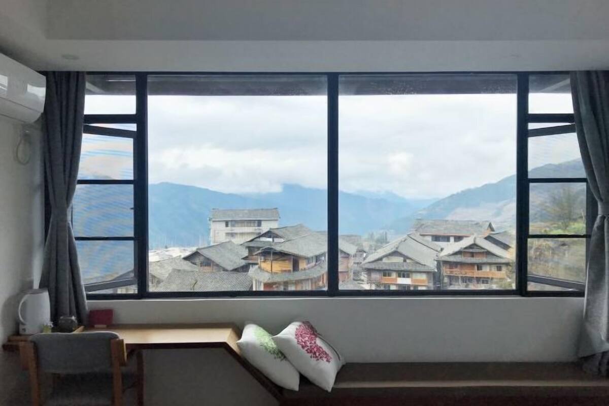 A room with a large window overlooking a mountainous village.