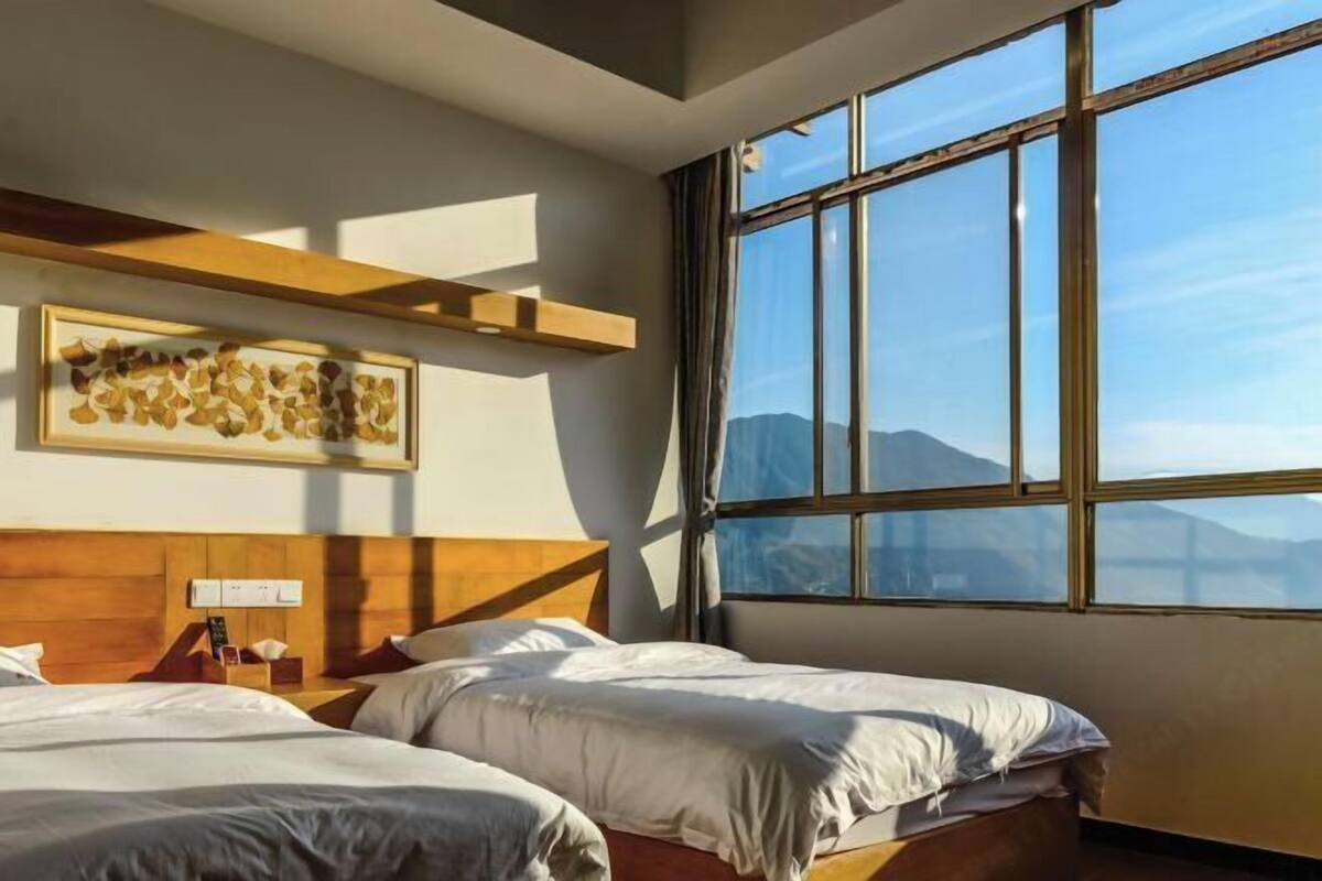 A hotel room with two beds, a large window with a mountain view, a wooden headboard, and a wall-mounted artwork.