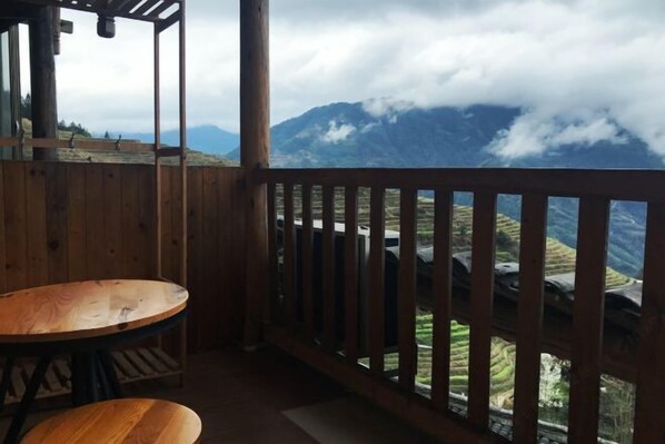 Um deck de madeira com mesa e cadeiras, com vista para campos em socalcos e montanhas.