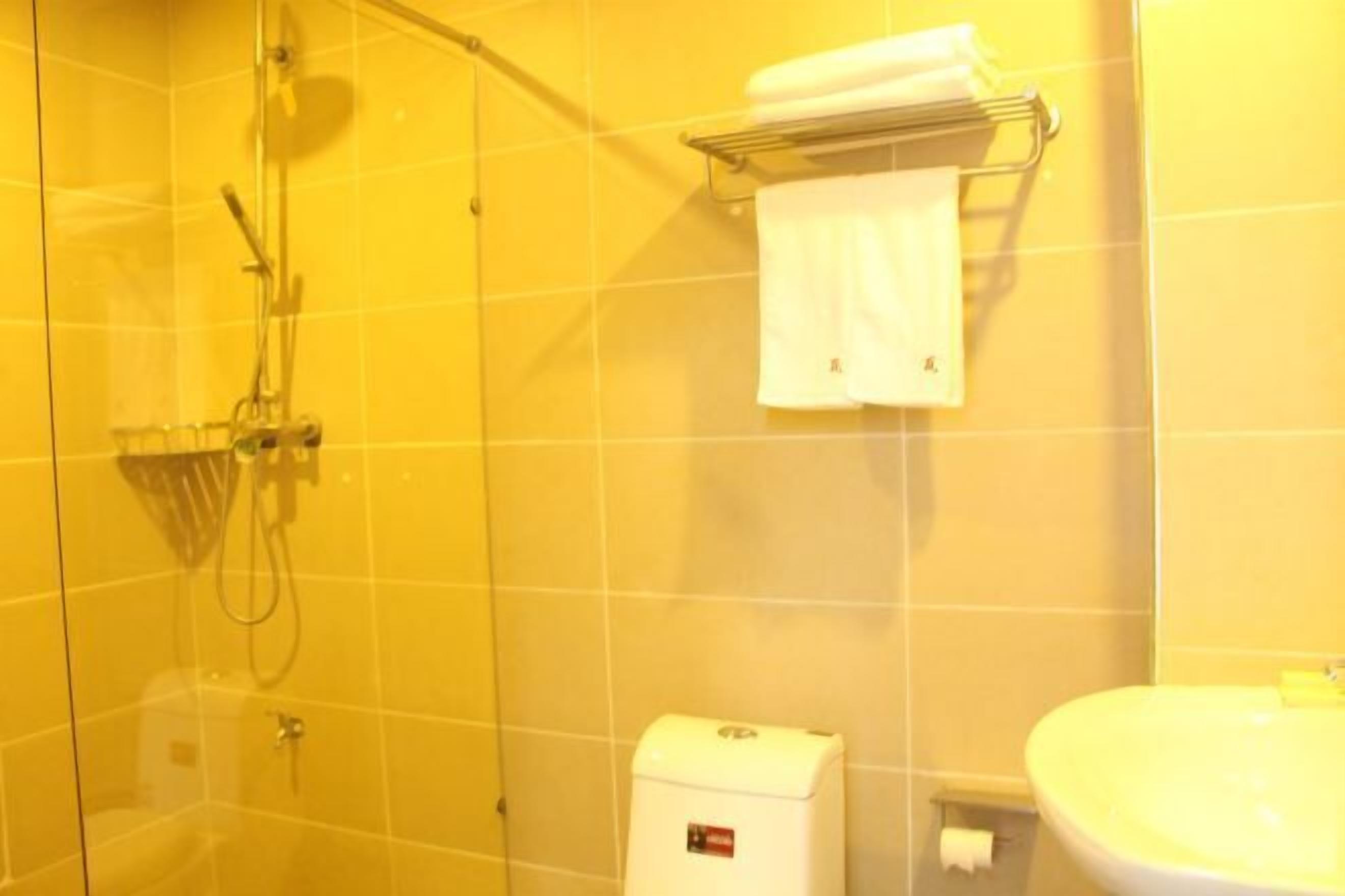 A bathroom with yellow tiles, a glass shower enclosure, a white sink, and a towel rack.