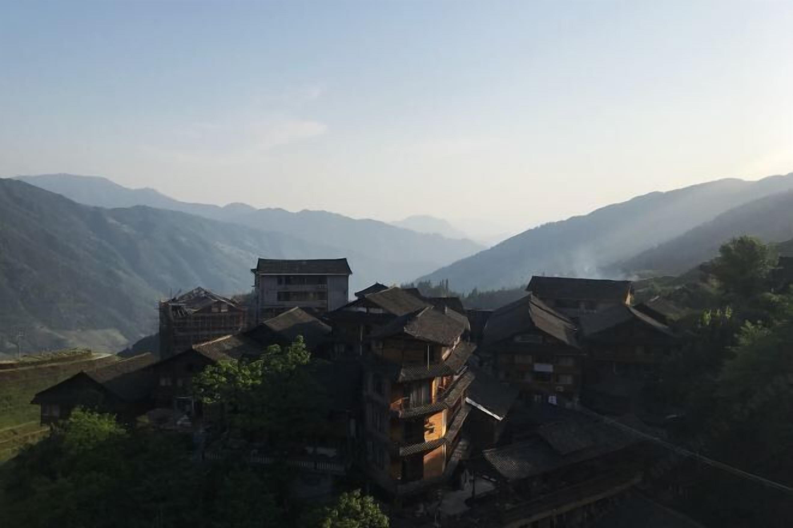 A traditional village with multi-story buildings, some with visible balconies, set against a backdrop of mountains.