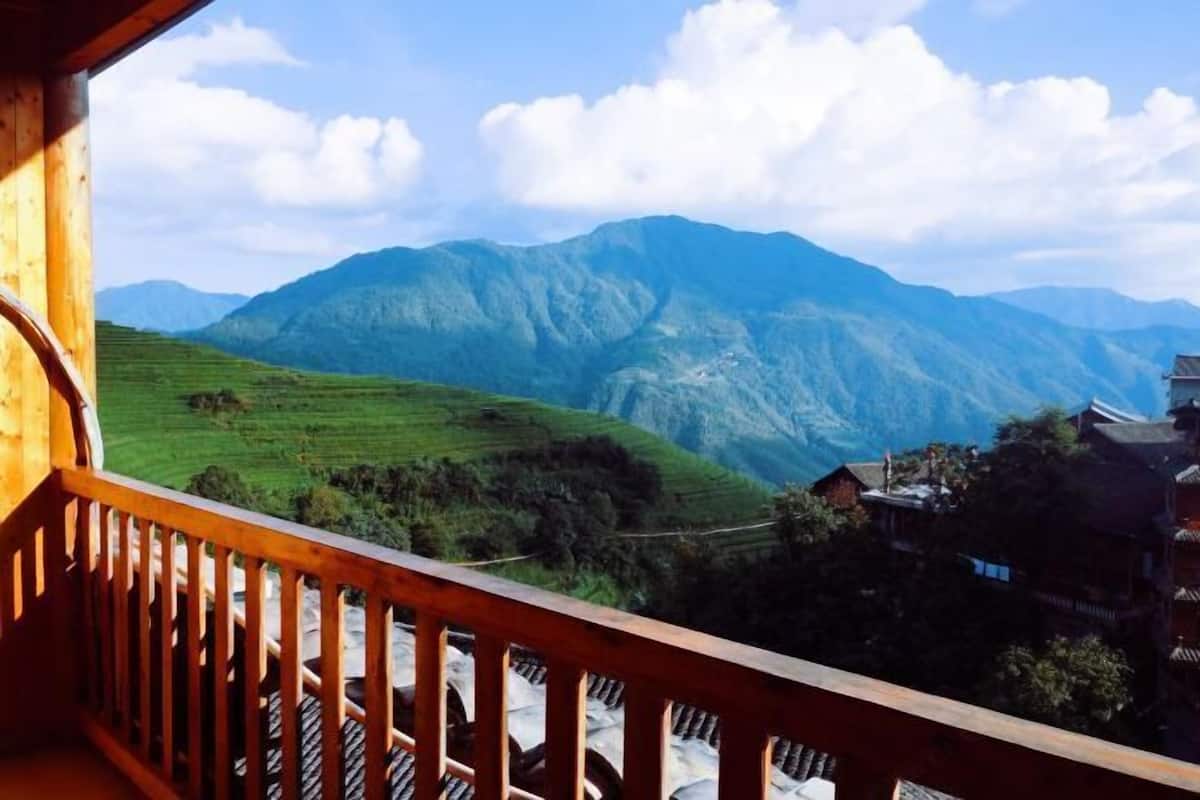 A wooden balcony with a view of green hills and mountains.