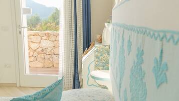 A bedroom with a bed, a window with curtains, a stone wall outside, and a view of the outdoors.