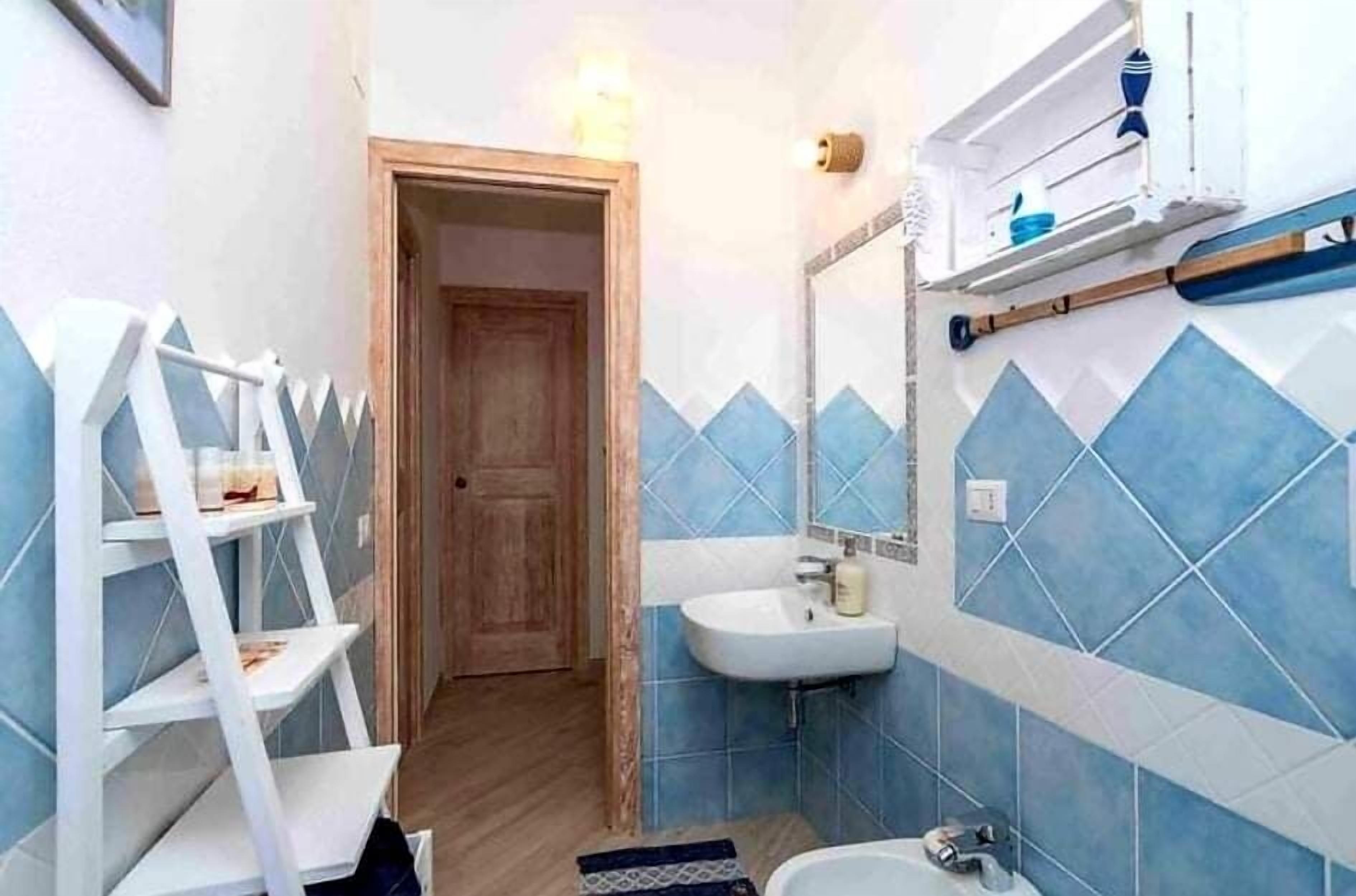 Une salle de bain avec des murs recouverts de carreaux bleus, un lavabo blanc et une porte en bois.