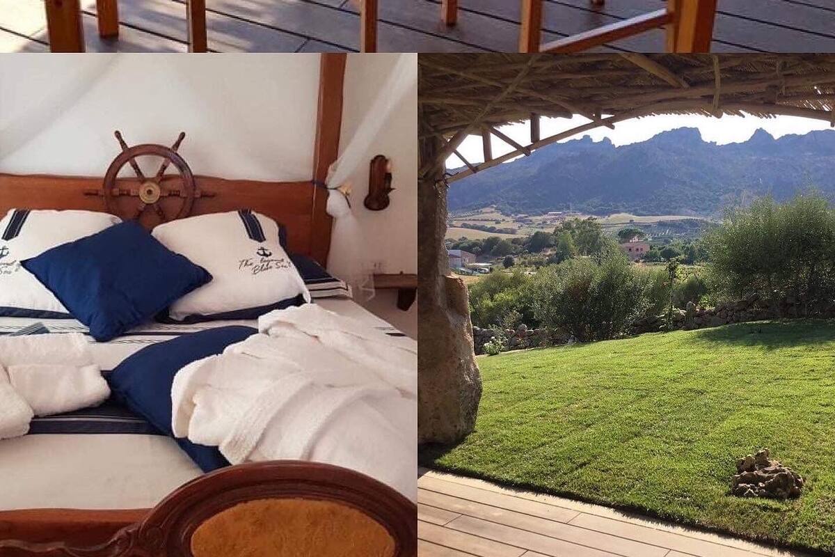 A wooden deck with a table and chairs, a small vase with flowers, and a view of a green landscape.