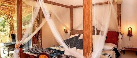 Ein Zimmer mit einem Himmelbett, Holzböden und Blick ins Freie.