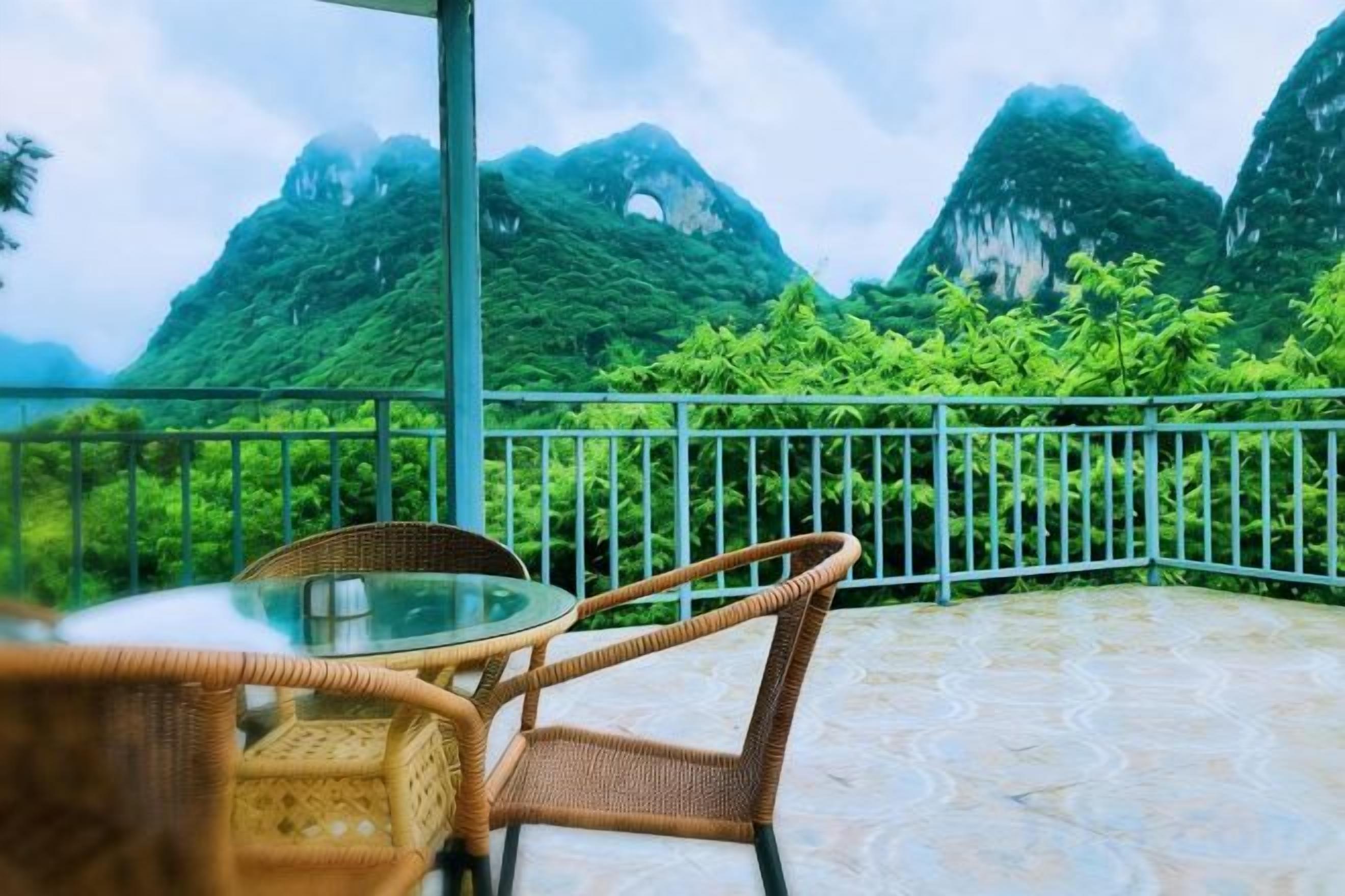 A balcony with wicker furniture, a glass table, and a view of green mountains.