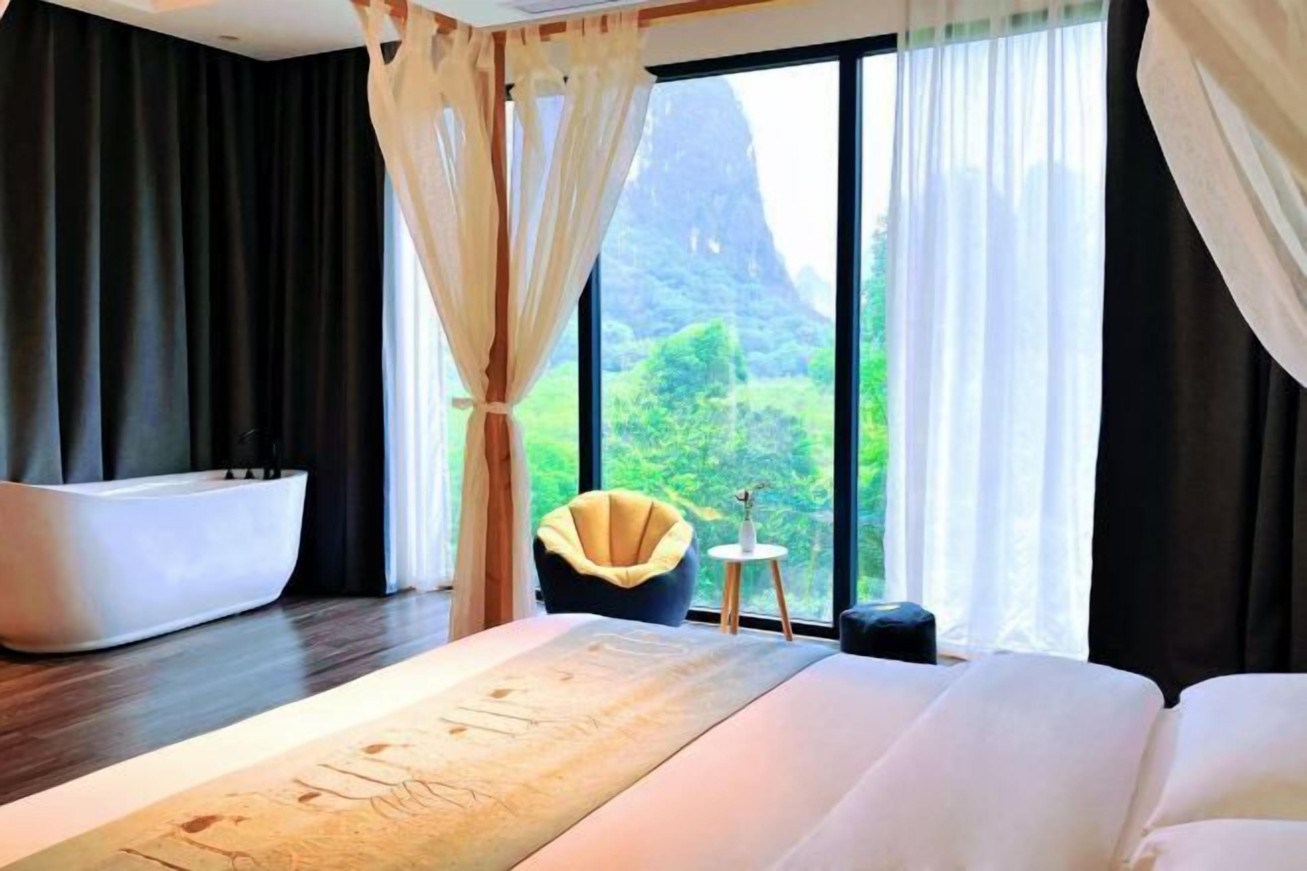 Una habitación de hotel moderna con una cama grande, una bañera y vistas a zonas verdes y una montaña.
