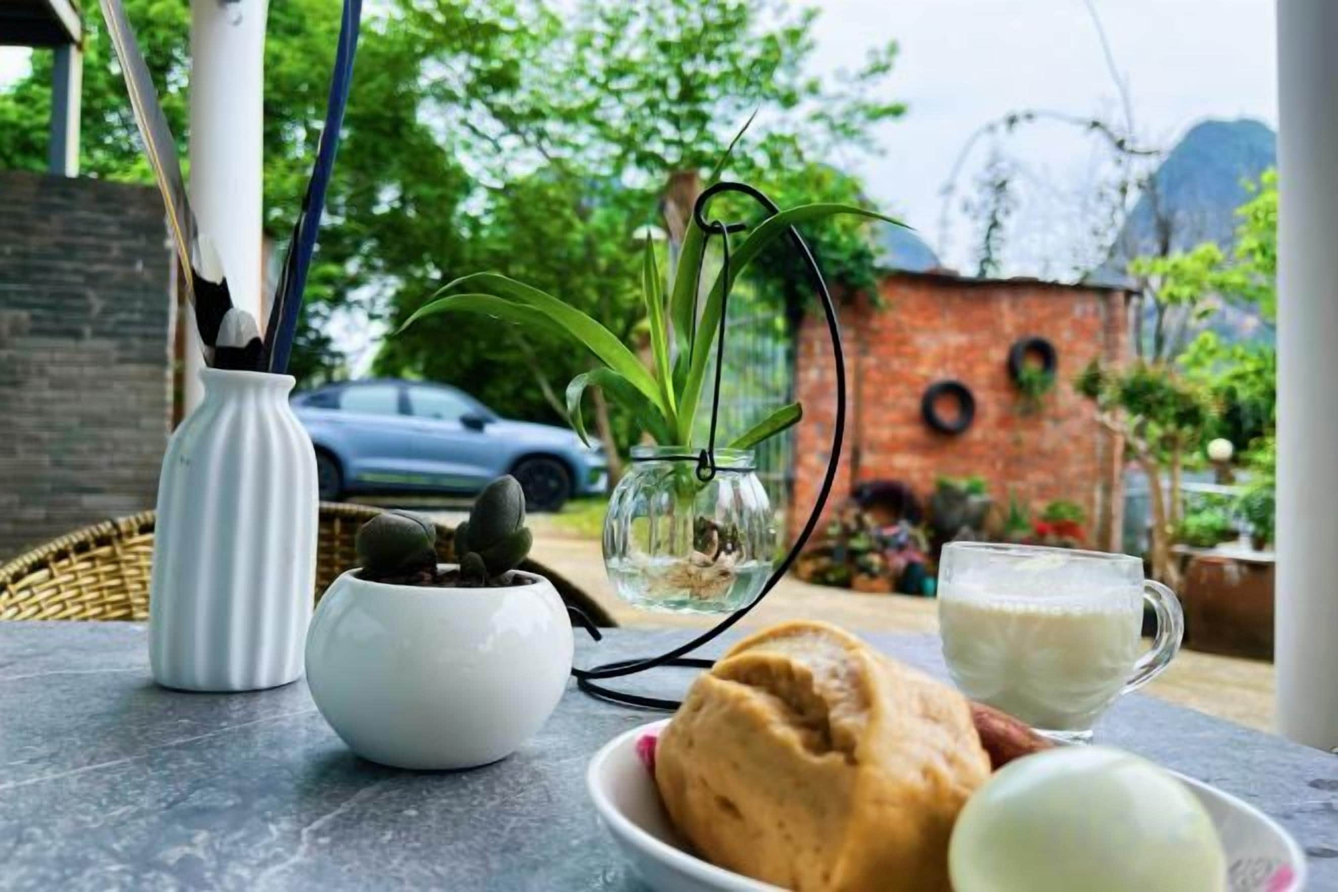 A table with a glass of milk, a bowl of bread, a potted plant, and a white vase.