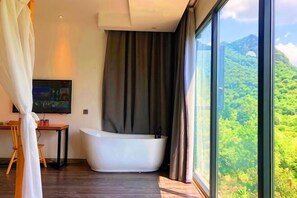 Une salle de bain moderne avec une baignoire sur pieds, un téléviseur et une grande fenêtre donnant sur un paysage montagneux.