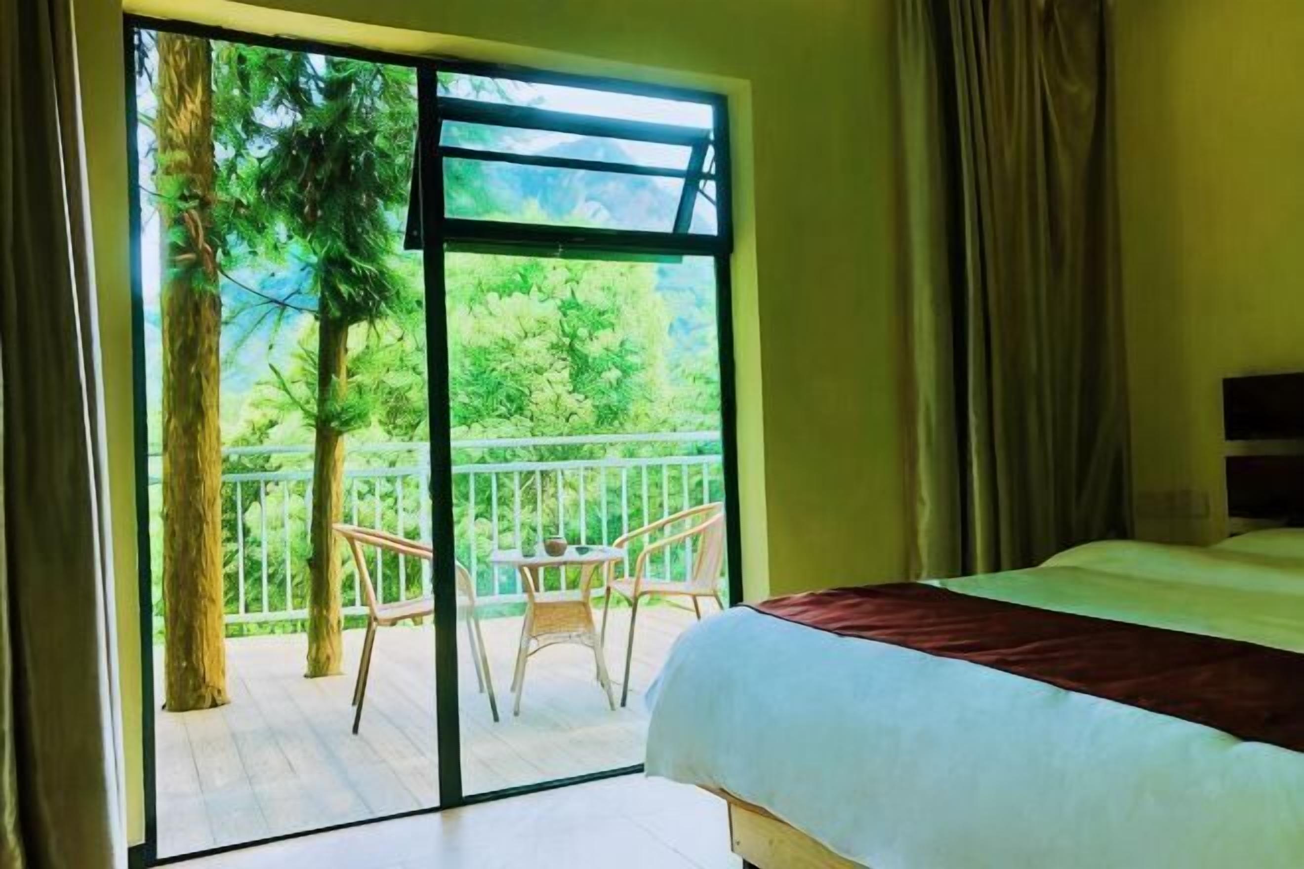 Ein Schlafzimmer mit Bett, einem Balkon mit Stühlen und Blick auf Grünflächen.