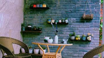 Una habitación con pared de ladrillo, muebles de mimbre y estantes con plantas y adornos.