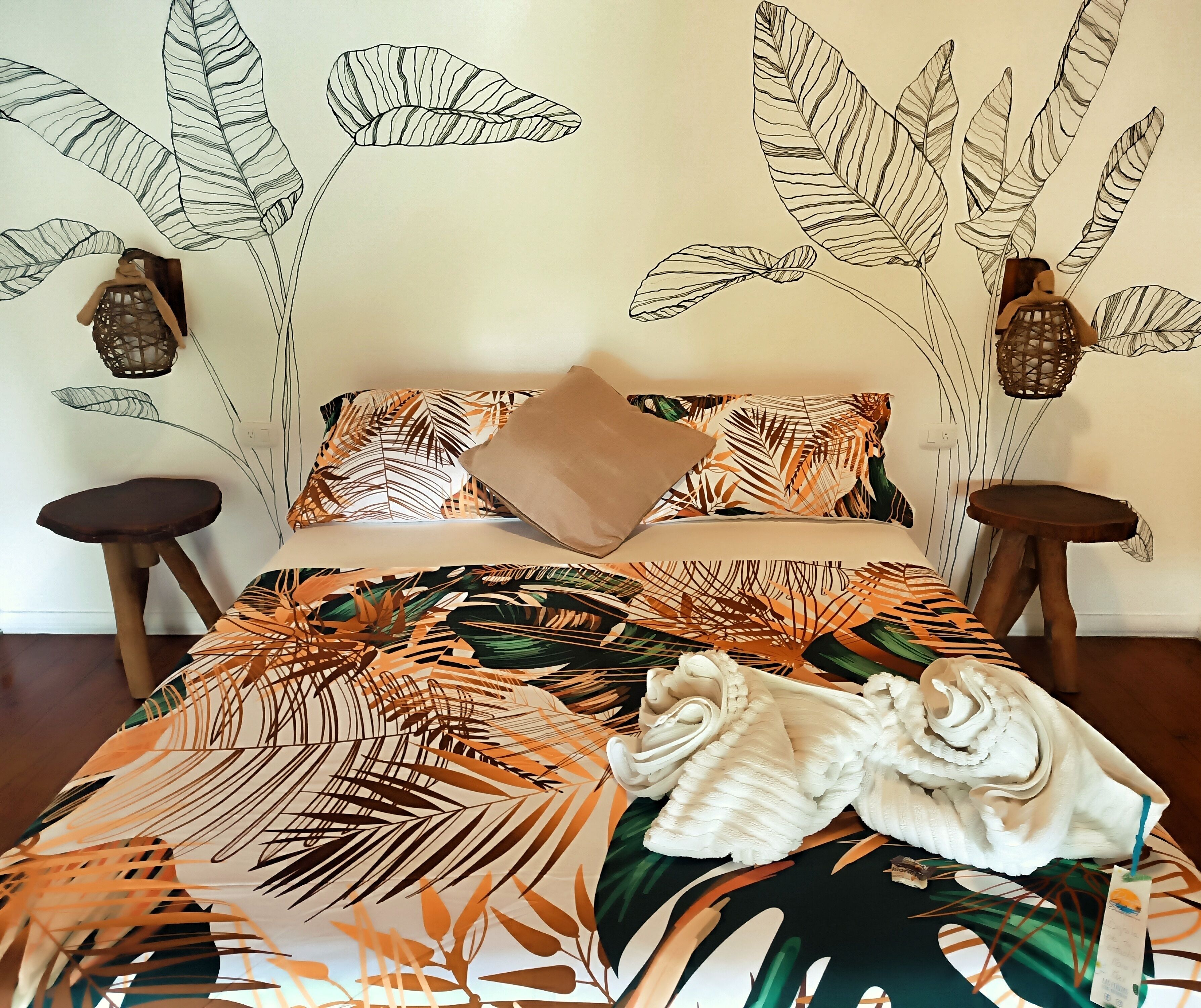 A bed with a tropical leaf pattern bedspread, two nightstands, and wall art with leaf designs.