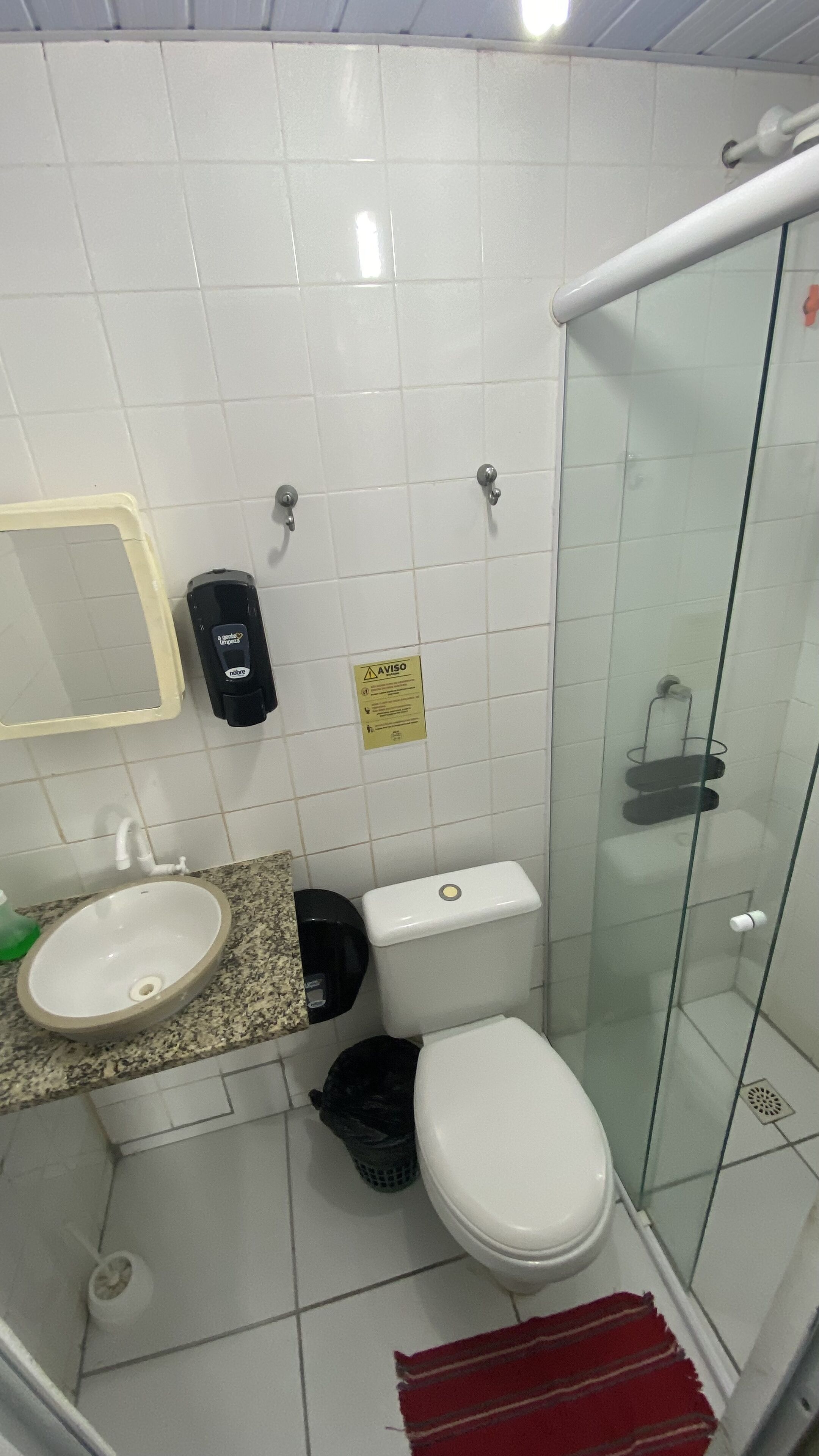 Un baño con inodoro blanco, lavamanos, cabina de ducha de vidrio y secamanos.