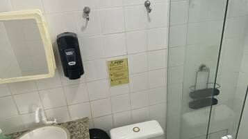 Un baño con inodoro blanco, lavamanos, cabina de ducha de vidrio y secamanos.