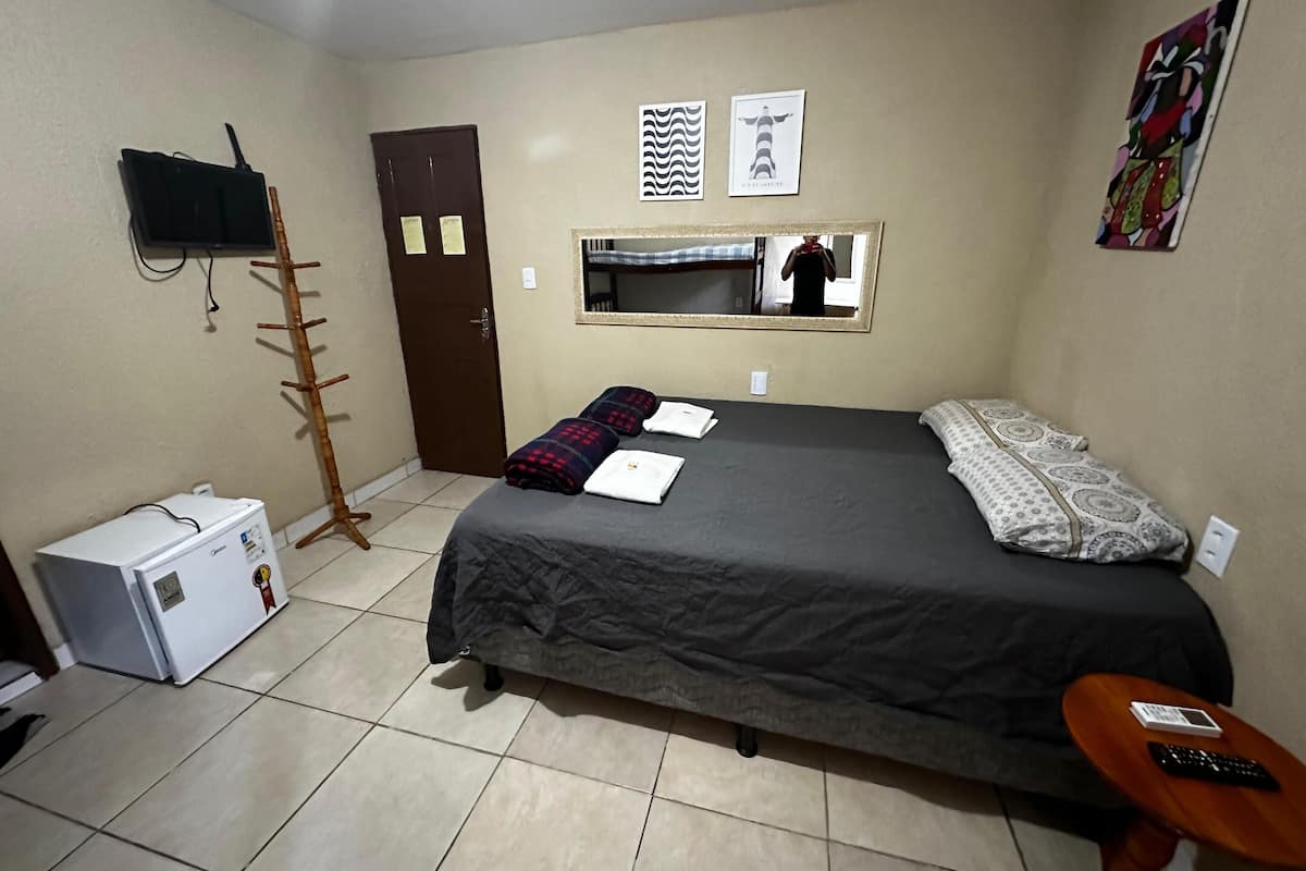 Slaapkamer met een bed, een klein tafeltje, een stoel, een garderobe, een spiegel en een tv aan de muur.