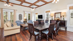 A spacious living room with a large wooden dining table surrounded by chairs, a beige sofa, and a television on a stand. - WaterColor Park District - Private beach access & amenities! (Santa Rosa Beach)