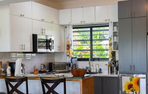 A kitchen with white cabinets, a microwave, a toaster, and a window with a view of greenery.